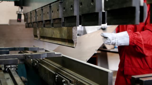 worker bends a sheet of metal using a metalworking machine
