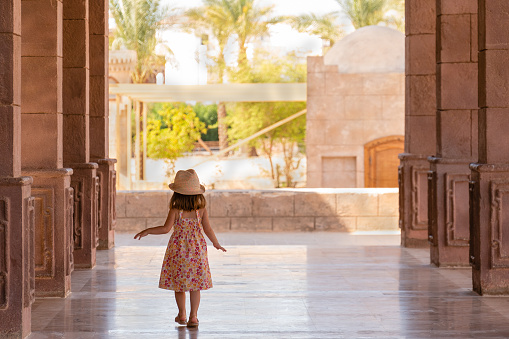 Pretty little girl walks slowly down the portico among the columns. Rear view. El Mustafa Mosque, Sharm El Sheikh, Egypt.