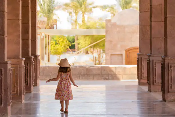Photo of Pretty little girl walks slowly down the portico among the columns