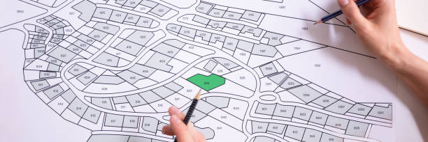 istock Human Hand Holding Pencil Over Cadastre Map 1364959149