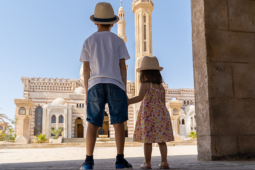 A boy and a girl standing in front of El Mustafa Mosque holding hands and looking at it. View from behind. Sharm El Sheikh, Egypt.