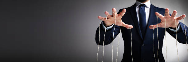 Man's Hand Controls The Puppet With The Fingers Attached To Threads Against Gray Background
