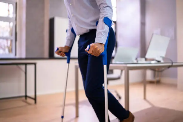 Worker With Crutches At Workplace Or Office. Handicap Rehabilitation Benefits