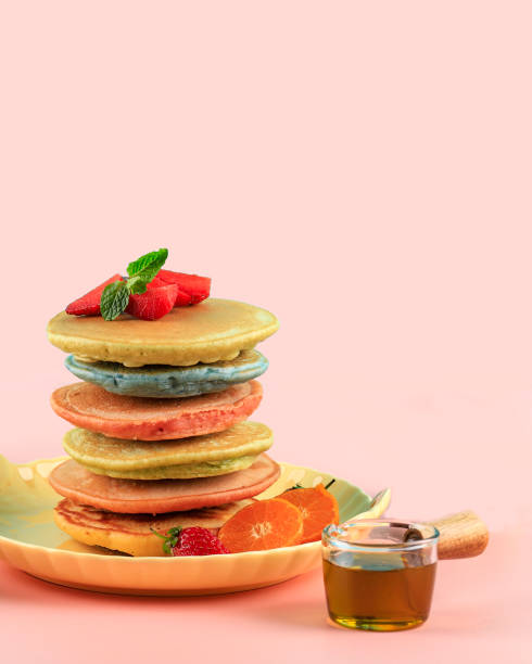 Pancakes Stack with maple syrup and raspberries isolated on a pink background. Family Breakfast.
