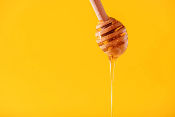 istock honey flowing from a wooden spoon on a yellow background with space for text 1364965569