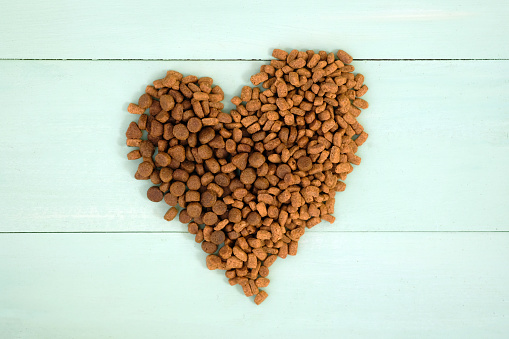 Dry food for dogs and cats on a wooden painted background top view. Dry pet food laid out in the shape of a heart.