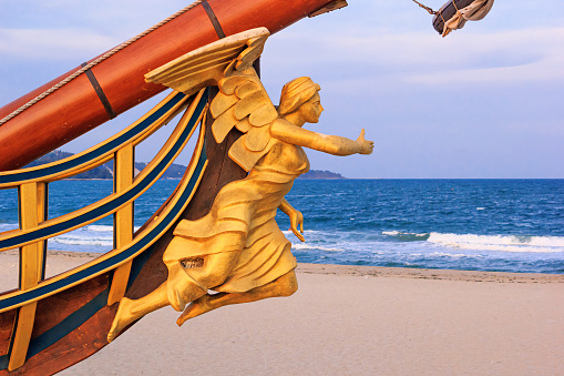 View of the bow and the figurehead of a stylized vintage sailboat close-up against the backdrop of the beach in Varna, on the Black Sea coast of Bulgaria