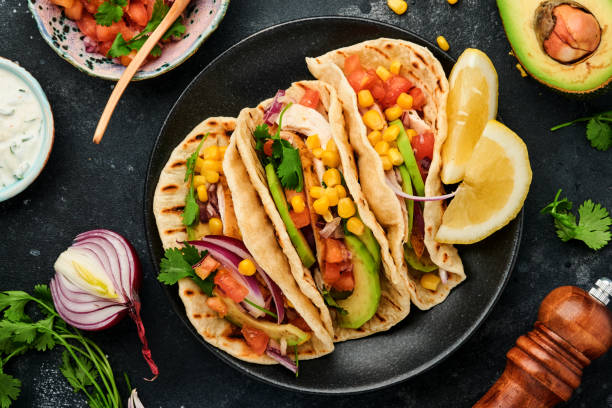 istock Mexican tacos with grilled chicken, avocado, corn kernels, tomato, onion, cilantro and salsa at black stone table. Traditional Mexican and Latin american street food. Top view. 1364988458