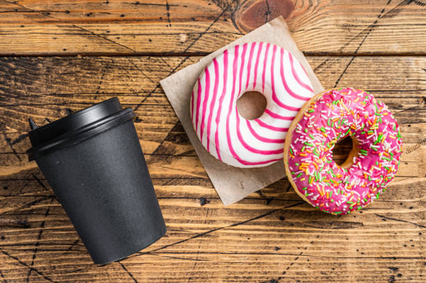 istock Pink glazed donuts on a kitchen table with coffee. Wooden background. Top view 1364988537