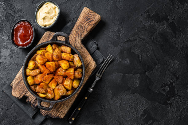 patatas bravas, pommes de terre épicées, un plat espagnol avec des pommes de terre frites et une sauce à l’ail épicée. fond noir. vue de dessus. espace de copie - patatas bravas photos et images de collection