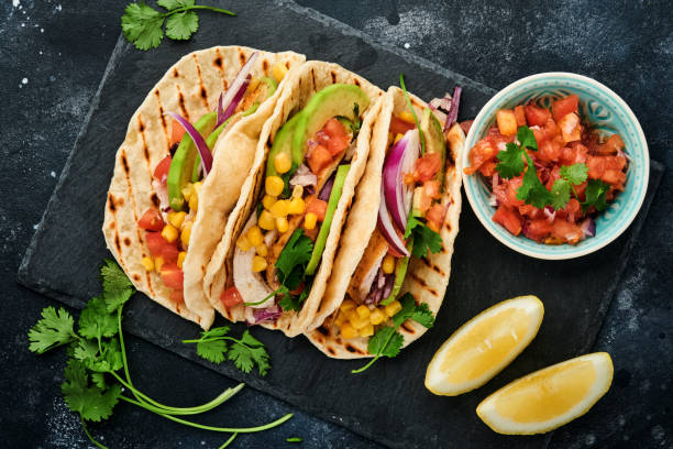 istock Mexican tacos with grilled chicken, avocado, corn kernels, tomato, onion, cilantro and salsa at black stone table. Traditional Mexican and Latin american street food. Top view. 1364988580