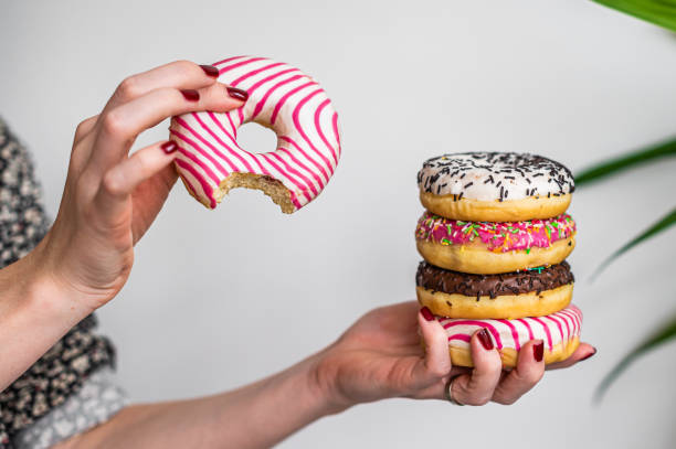 istock Female holds in hand colorful stack of glazed donuts. White background. Top view. Copy space 1364989070