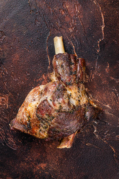 istock Roast Lamb leg with herbs and garlic. Dark background. Top view 1364989884