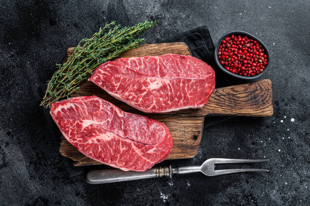 Fresh Raw Top Blade or flat iron beef meat steaks on a butcher cutting board. Black background. Top View Fresh Raw Top Blade or flat iron beef meat steaks on a butcher cutting board. Black background. Top View. boneless chuck steak stock pictures, royalty-free photos & images