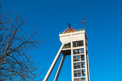 Cityscape of Silesia. Shaft tower with a red hoisting wheel and a bare tree against clear blue sky.