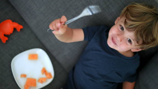 istock Happy child eating melon fruit sitting on sofa looking at camera 1364991334