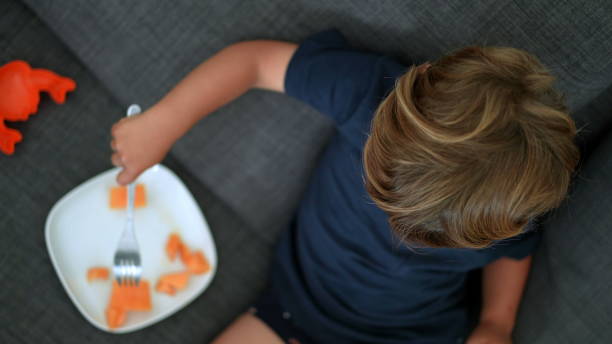 istock Happy child eating melon fruit sitting on sofa looking at camera 1364991374