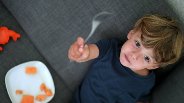 istock Happy child eating melon fruit sitting on sofa looking at camera 1364991477