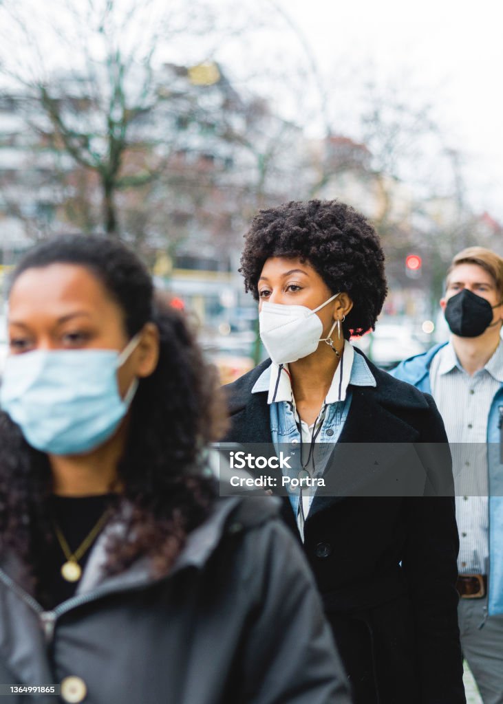 People standing at temperature checkpoint line outside office Woman standing in a line at temperature checkpoint outside office building. People wearing protective face masks standing in queue at office entrance for body temperature checkup during covid-19 pandemic. Protective Face Mask Stock Photo