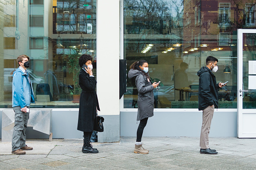 Side view of a people standing in a line at temperature checkpoint outside office building. People wearing protective face masks standing in queue at office entrance for body temperature checkup during covid-19 pandemic.