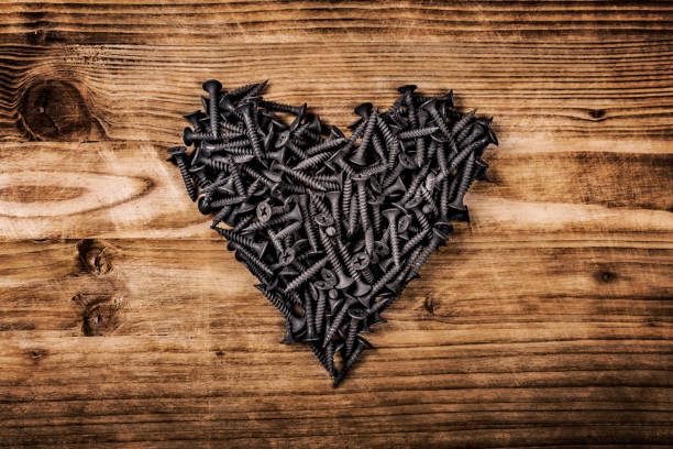 фигура в форме сердца, выложенная из винтов на винтажной коричневой деревянной доске. концепция металлической искусственной сердечной маш - rust free стоковые фото и изображения