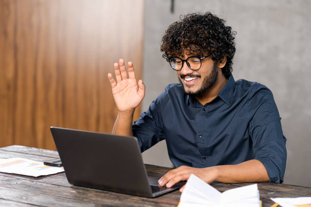 istock Video call concept, virtual meeting. Young middle eastern guy relaxed sitting at the table and talking online via video call with group of friends or employees 1364993158
