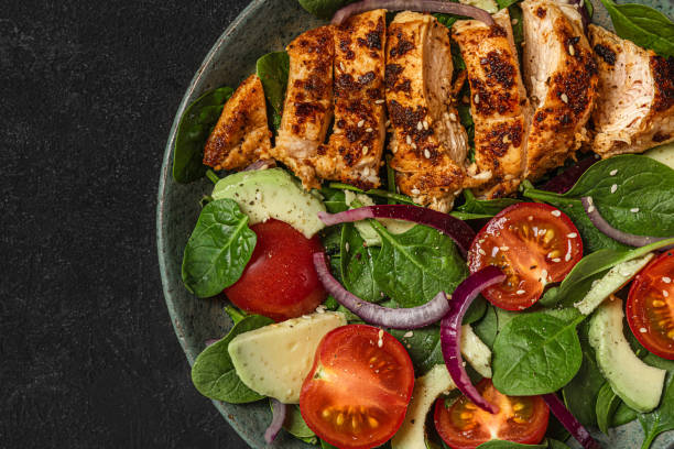 istock Fresh salad with chicken breast, spinach, avocado, sesame seeds and tomato on black background. Top view. close up 1364995572