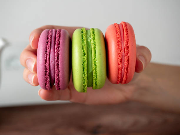 istock Close-up of a woman's hand holding three colorful macaroons. Front view 1364995837