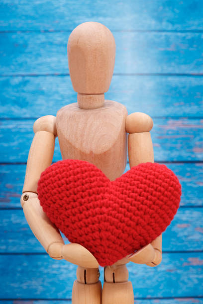 istock wooden man keeps his heart on a blue background 1364996079