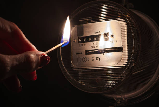 A burning matchstick in complete darkness near a home electricity meter during a power outage. stock photo