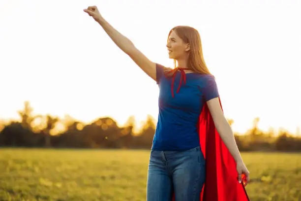 Superhero woman. A young and beautiful blonde in the form of a superheroine in a red cloak is growing Forward and upward. Woman dressed as a superhero in nature. Feminism concept