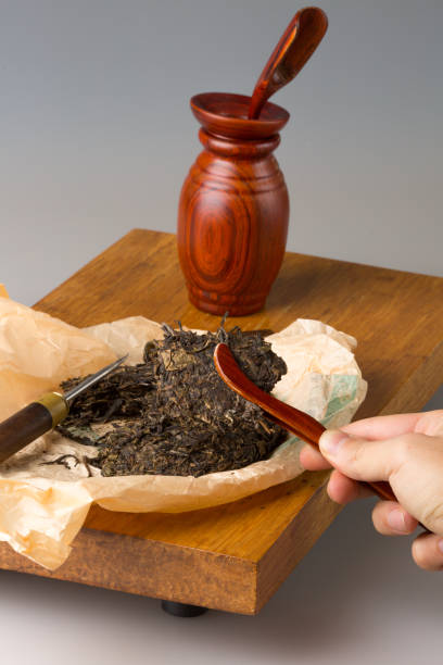 istock Wooden table for tea ceremonies and a set for brewing tea. Pressed pu-erh tea on the table. A man's hand separates pieces of tea leaves and puts them in a teapot with a spatula 1365004981