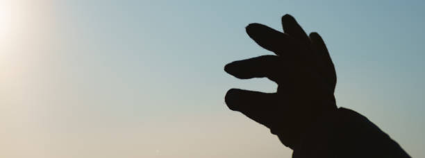 istock Blurred sunset without clouds. Sky paints in soft orange and blue. Winter nature. Back light photography. Fingers of a female hand. She's trying to take the sun disk.  Concept of unity with nature 1365007483
