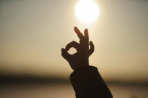 istock Blurred sunset with fog without clouds. Sky paints in orange. Soft focus, motion blurred. Winter nature. Back light photography. Human hand with OK gesture. Concept of unity with nature 1365007540