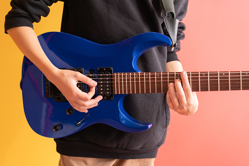 Close up funky boy playing electric guitar over colored background