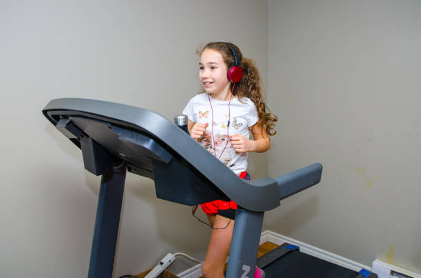 Girl jogging on home exercise treadmill in the basement without running shoes, wearing socks, shorts, t-shirt and pony tail. She's listening music with headphones.