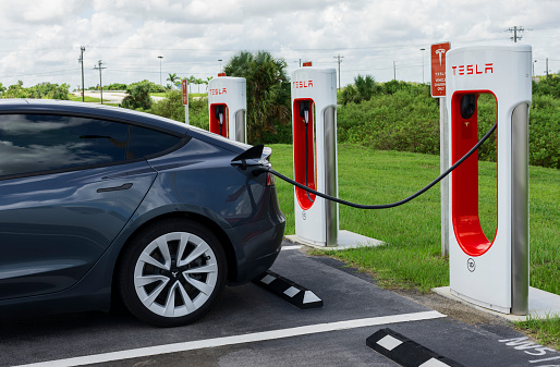 Miami, Florida, USA - August 29, 2021:  Tesla Model Y electric car at Tesla Supercharger charging station. The charging station and grey Tesla Model Y is plugged in with a cable.