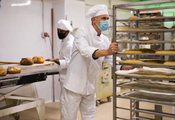 istock Male baker carrying rack trolley with bread 1365013115