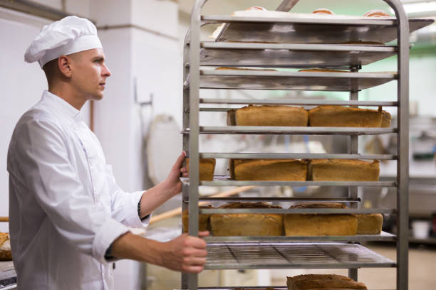 istock Male baker carrying rack trolley with bread 1365013118