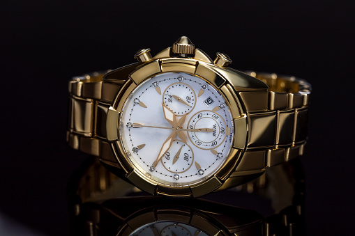 golden ladies watch with a metal bracelet, chronometer, precious stones, diamonds on a black background with reflection. The concept of an expensive gift for women, luxury. Close-up, macro. High quality photo