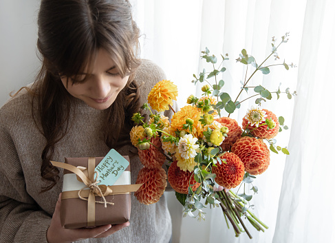 Attractive young woman with a mother's day gift and a bouquet of chrysanthemum flowers in her hands.