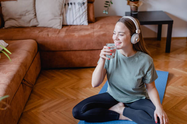 Young woman drinks water at home after home exercise