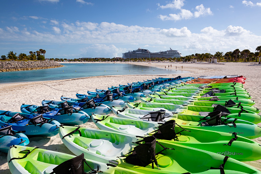 Ocean Cay, Bahamas - January 3, 2022: Rows of unused kayaks line the beach at Ocean Cay MSC Marine Reserve in the western Bahamas. A cruise ship, the MSC Meraviglia, is docked in the distance. Due to the ongoing pandemic, the island was receiving fewer visitors than normal.