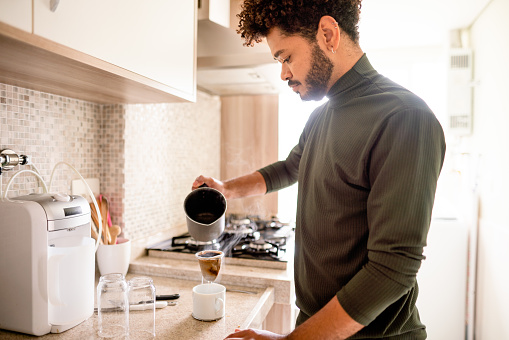 Young man making freshly brewed coffee at home