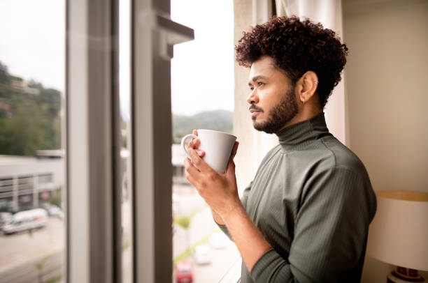istock Young man drinking coffee while looking out of a window at home 1365018249