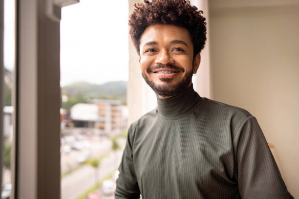 istock Smiling young man standing by a window at home 1365018793