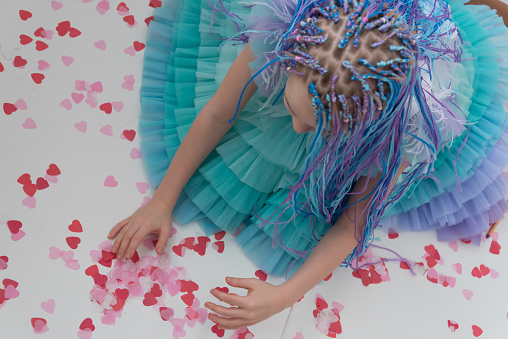 A teenage girl in a beautiful evening puffy dress collects confetti from hearts. Concept, Valentine's Day. View from above.