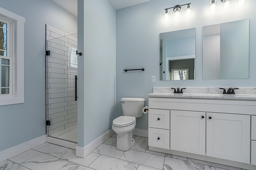 Real estate photography photograph of a farmhouse style bathroom with white cabinets, granite counter tops, tile floor, subway tile shower, and blue walls.