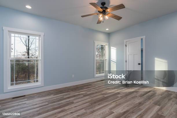 Real Estate Photography Photograph Of An Empty Master Bedroom With The Farmhouse Style Finishing Wooden Floors Blue Walls Two Windows Looking Out Over A Forest And A Slightly Open Door Leading To A Closet Stock Photo - Download Image Now