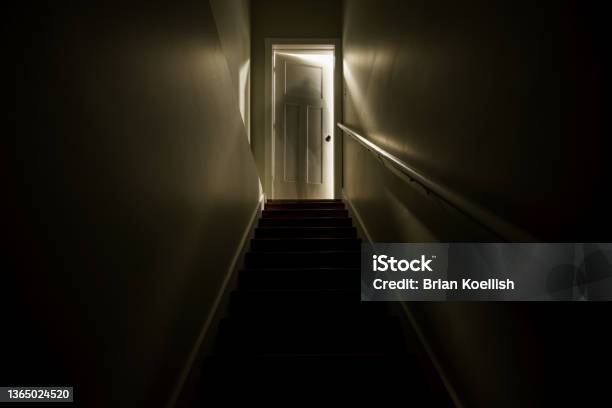 A Dark Stairwell Illuminated By A Slightly Opened Door At The Top Of The Stairs Shot With A Long Exposure To Create The Effect Of A Sillhouette Of A Ghost Like Figure At The Top Of The Stairwell Stock Photo - Download Image Now
